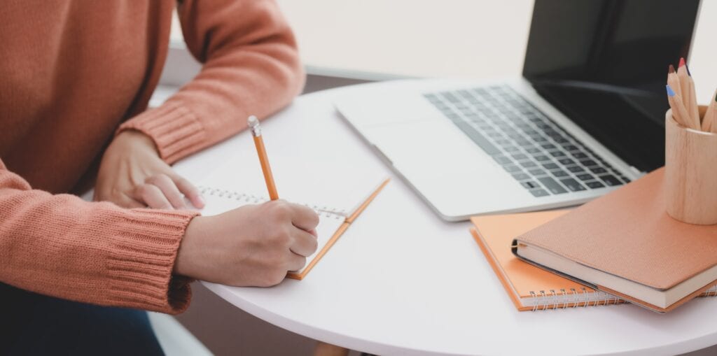 person at computer writing in notebook